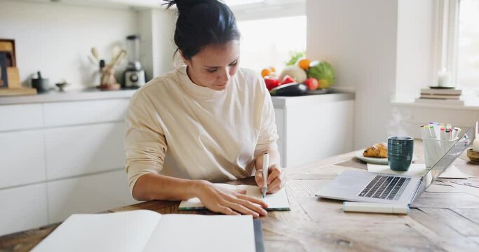 Young woman drawing designs in a sketchbook while sitting at a table in her kitchen at home