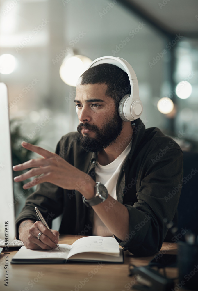 Poster Steady focus takes you further. a young businessman writing in a notebook and using a computer with headphones during a late night at work.