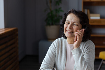 Fototapeta na wymiar Happy middle aged senior woman talking on smartphone with family friends. Older mature lady with cell phone chatting with grown up children, resting in at home. Older generation modern tech usage