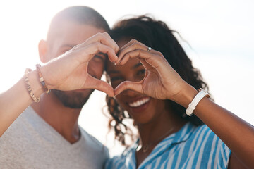 Youll always be in my heart. a young couple making a heart shape with their hands at the beach.
