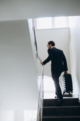 A businessman with a suitcase is walking up the stairs in the hotel.