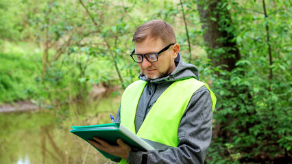 Fototapeta premium Man ecologist in the forest near a reservoir makes marks of control of the ecological situation of the environment.