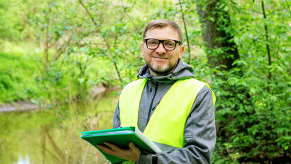 Portrait of a male ecologist in the forest near a reservoir, controls the ecological situation of the environment. Biology teacher. - obrazy, fototapety, plakaty