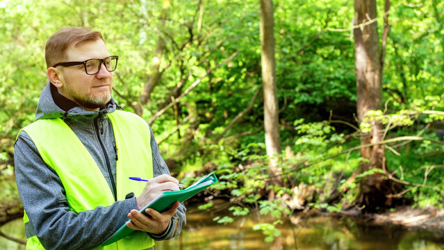 Man ecologist in the forest near a reservoir makes marks of control of the ecological situation of the environment.