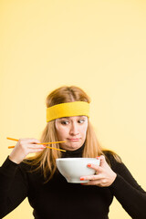 I have no idea how to use chopsticks. an attractive young woman standing alone in the studio and eating with chopsticks.