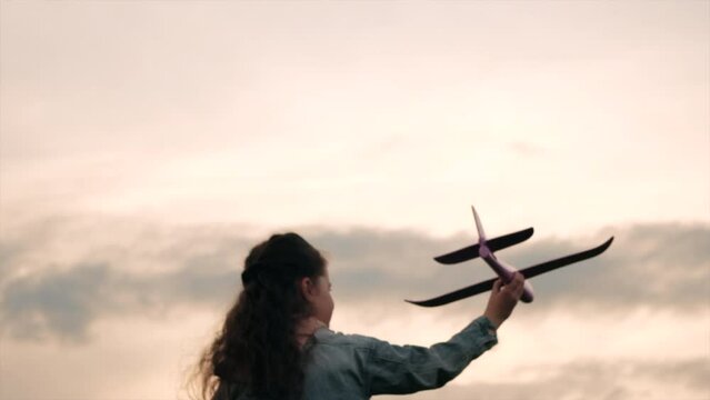 Selective focus of happy little girl kid walking with an airplane on background sunset and amazing cloudy sky. Dream freedom airplane concept. Playful child run on field holding in hands toy aircraft