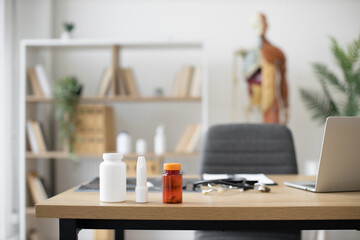 Close up view of medicine bottles and plastic vial placed on writing desk near computer and stethoscope at doctor's office. Modern workplace for healthcare practitioner at private clinic.