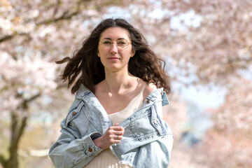 Portrait of a young tender woman against the backdrop of cherry blossoms. Dark natural hair flutters beautifully in the wind. Natural beauty of a girl. Without makeup.