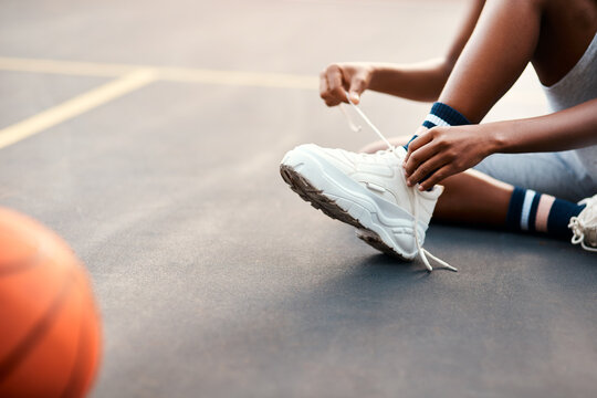 Making sure my laces are tied. an unrecognizable sportswoman sitting on the court and tying her shoelaces before playing a game of basketball.
