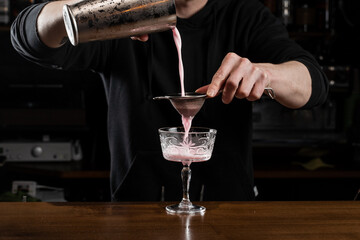 Bartender is pouring pink Clover club alcoholic cocktail in the glass. Bartender mixes egg white, lemon, dry vermouth and gin to prepare the Clover club cocktail.