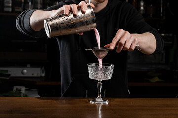 Bartender is pouring pink Clover club alcoholic cocktail in the glass. Bartender mixes egg white, lemon, dry vermouth and gin to prepare the Clover club cocktail.
