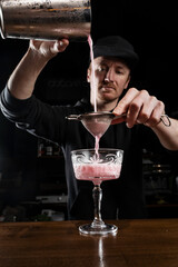 Bartender is pouring pink Clover club alcoholic cocktail in the glass. Bartender mixes egg white, lemon, dry vermouth and gin to prepare the Clover club cocktail.