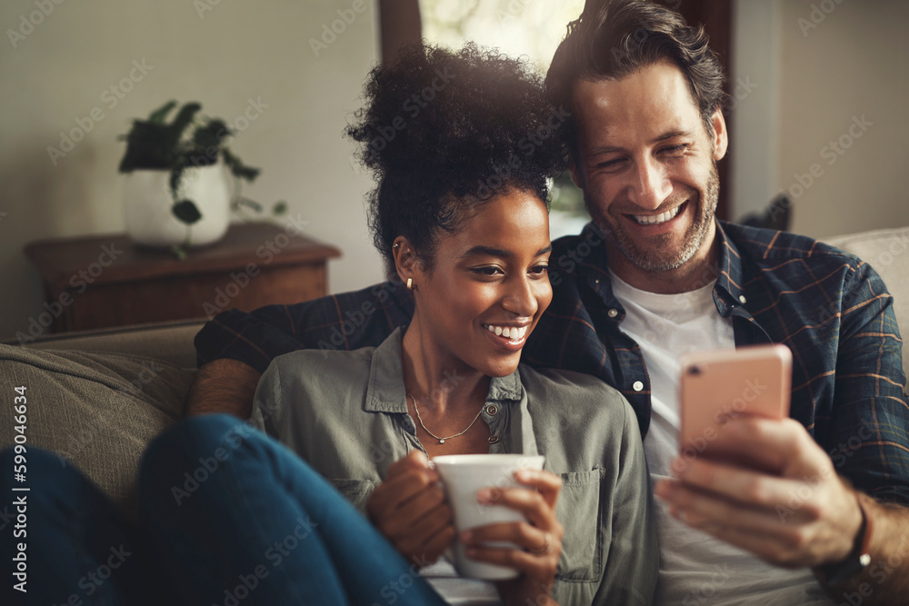 Poster Look at these messages with me. a happy young couple using a cellphone together while relaxing on a couch at home.