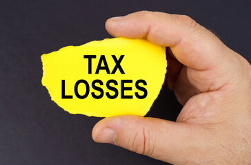 On a black background, in the hands of a man, a yellow torn cardboard with the inscription - tax losses