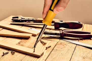 Hand holding tool in the workshop. Screwdriver, flat file, pliers, monkey wrench, screws and boards...