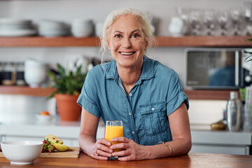 Its not breakfast without a vitamin C boost. a mature woman having orange juice with her breakfast in the kitchen at home.