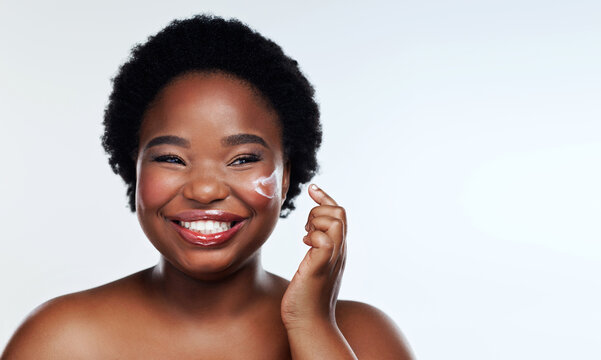 The moisturiser that keeps my skin happy. Studio shot of a beautiful young woman applying moisturiser to her face against a gray background.