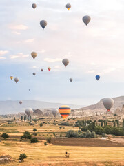 Fototapeta na wymiar Flying in sky many bright colored beautiful balloons into air in Cappadocia in mountains early at sunrise, dawn. Filling balloon with hot air from burner, big basket. Tourists excursion, cloud flight
