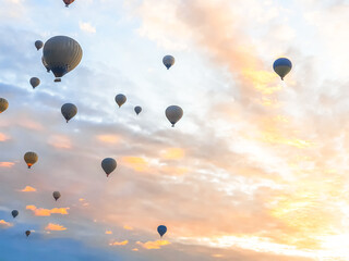 Flying in sky many bright colored beautiful balloons into air in Cappadocia in mountains early at sunrise, dawn. Filling balloon with hot air from burner, big basket. Tourists excursion, cloud flight