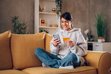 Woman using smartphone and holding credit card while online shopping from home