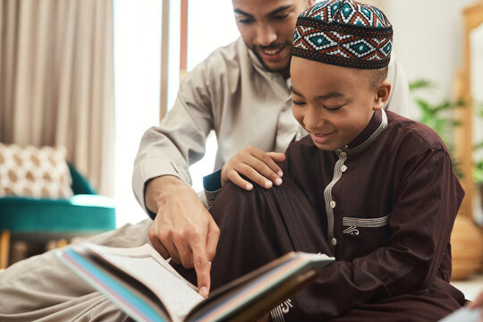 A reader lives a thousand lives before he dies. a young muslim man and his son reading in the lounge at home.