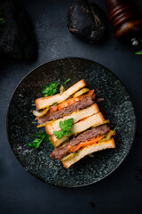 Sandwich with beef cutlet, pickled cucumber, tomatoes, lettuce and greens on dark background.