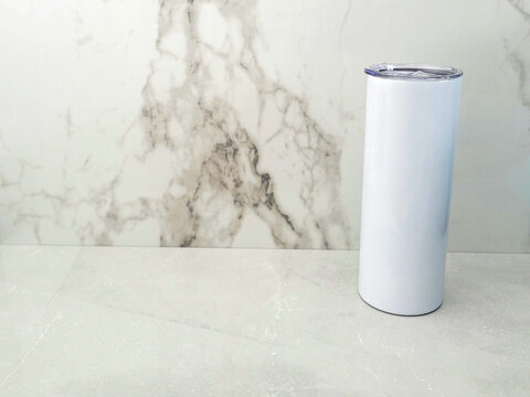 20oz blank tumbler off center against marble backdrop and marble surface.
