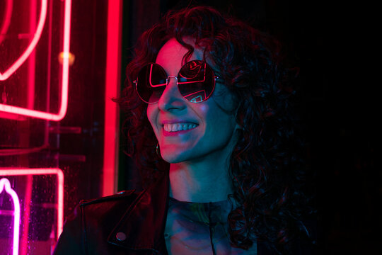 Portrait of a young girl in sunglasses in the night city, with creative light on the background of neon lamps