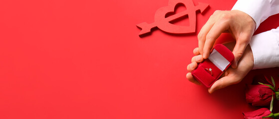Hands of man holding box with engagement ring on red background with space for text