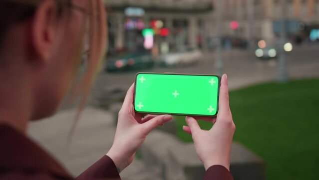 Young caucasian woman hands hold smart phone with horizontal green screen outdoors internet mobile smartphone technology city communication device use lifestyle slow motion