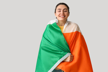 Young woman with flag of Ireland on grey background