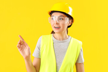 Female worker in vest pointing at something on yellow background