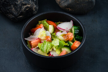 Green salad with cucumbers, lettuce, cherry tomatoes, and radish in a bowl.