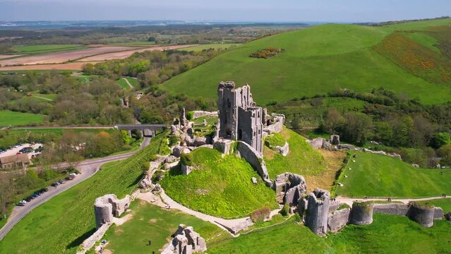 Aerial shot circling ruins of Corfe Castle on hill with scenery passing in the background on summer day