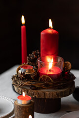 Rustic table decor for Christmas or New Year family dinner. Centrepiece with red candle, dry orange, cone, cinnamon, anise. Zero waste eco-friendly home. Cozy atmosphere, dark background. Close up