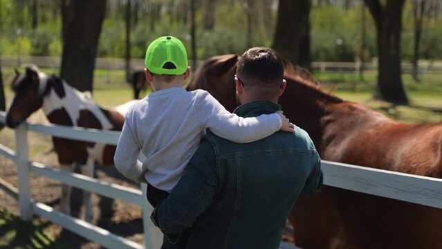 A father with a small son in his arms on a farm with horses Generative AI