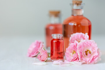 Composition with pure natural organic rose essential oil in glass bottle, luxury perfumery ingredient for premium fragrance, skin care products, anti-age beauty treatment. Fresh flowers