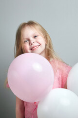 Little girl with balloon in pink knitted clothes on a gray background. Portrait of cute smiling girl, happy childhood