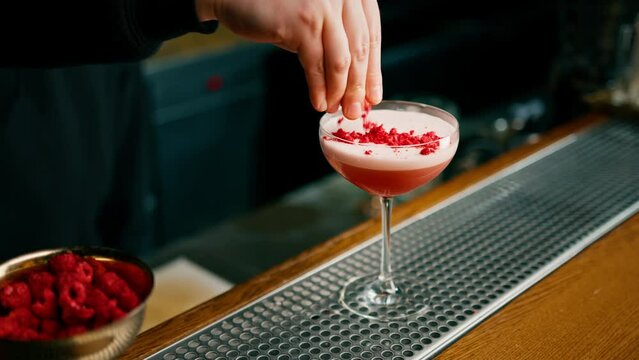 The bartender prepares a milk punch cocktail and puts chopped raspberries on top of the drink