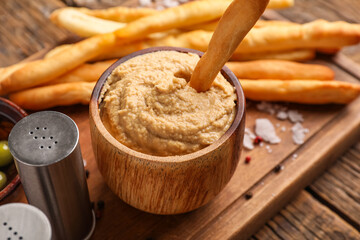 Bowl with tasty hummus and Italian Grissini on wooden background