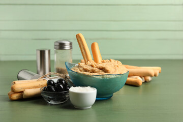 Bowl with tasty hummus and Italian Grissini on green wooden background