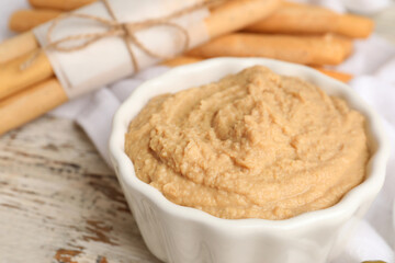 Bowl with tasty hummus on light wooden background, closeup