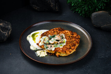 Fried potato pancakes with mushrooms, onions, greens and sauce in plate.