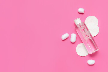 Bottle of micellar water with cotton balls and pads on pink background