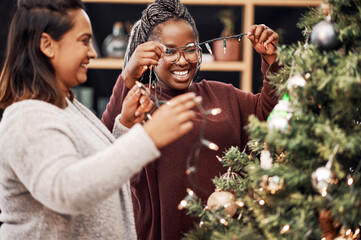 Christmas, here we come. two young women decorating a Christmas tree at home.