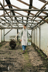 An attractive woman holding a tin bucket and walking in the greenhouse looking at seedlings