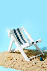 Deck chair with stylish jewelry and sand on blue background