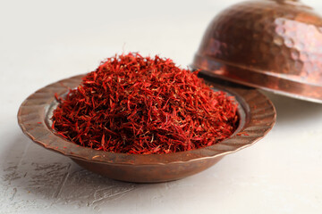 Bowl with pile of saffron on light background