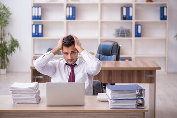 Young male employee and too much work at workplace