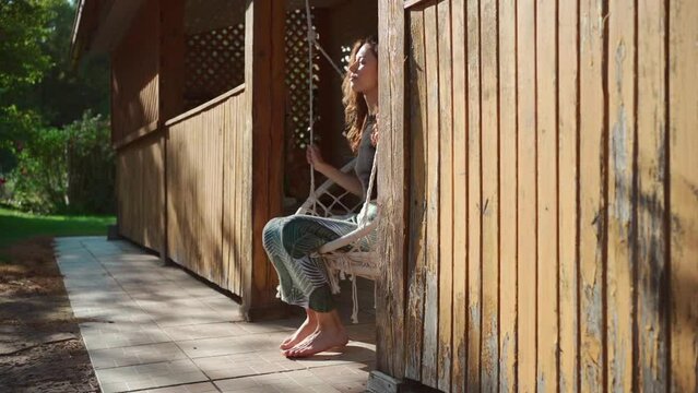 happy young female riding on macrame swing chair near country house outdoors Generative AI